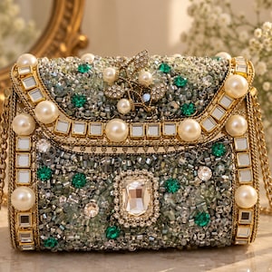 May include: A rectangular clutch bag featuring a gold metal frame, a gold chain strap, and an exterior covered in green and silver beads. The bag is decorated with large white pearls, square mirror tiles, and a central rectangular crystal.