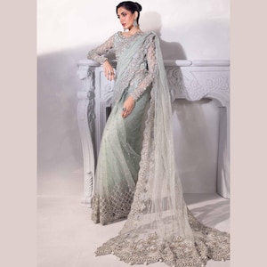 May include: A pale mint green saree featuring intricate silver embroidery and beadwork on the bodice and long sleeves. The sheer fabric drapes elegantly, showcasing a heavy, ornate border with detailed floral patterns and a long, flowing train.