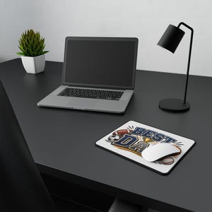 May include: A rectangular mouse pad featuring a white background with the text BEST DAD in bold blue letters. The design includes illustrations of a football, a soccer ball, a baseball, and a gold trophy. A white computer mouse rests on the pad.