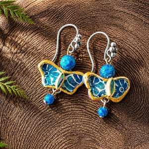 May include: A pair of butterfly-shaped earrings featuring blue patterned wings with gold-toned edges. Each earring includes a round blue bead at the top and a smaller blue bead dangling at the bottom, attached to silver-toned ear wires.