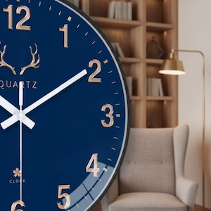 May include: A round wall clock with a deep blue face, featuring metallic rose gold numerals and a central deer antler emblem. The clock has white hour, minute, and second hands, with the text QUARTZ and CLOCK printed in rose gold on the face.