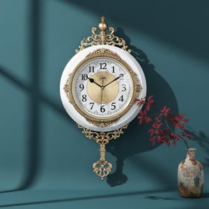 Peut inclure: Horloge murale blanche et dorée au design décoratif. Le cadran est blanc avec des chiffres et des aiguilles dorés. L'horloge a un cadre décoratif doré et un pendule. L'horloge est accrochée à un mur turquoise.