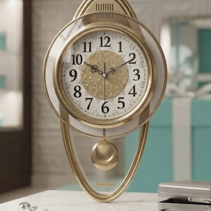 Peut inclure: Une horloge de cheminée dorée avec un cadran circulaire, des chiffres arabes noirs et un motif en filigrane doré au centre. L'horloge présente un pendule suspendu dans un cadre en forme de goutte et affiche le logo Tiffany & Co. à la base.