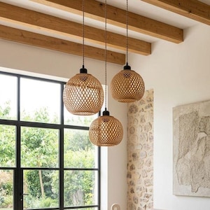 May include: Three pendant lights with woven, spherical shades hang from a light-colored ceiling. The shades are made of a light brown material, and the fixtures have black hardware. The lights are suspended in front of a large window.
