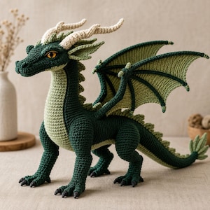 May include: A crocheted dragon toy featuring a dark green body with a light green underbelly, cream-colored horns, and large, textured wings. The creature has sharp black claws, a long tail, and bright yellow eyes with vertical pupils.