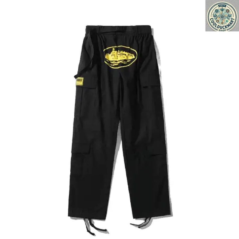 May include: Black cargo pants with a yellow oval design on the back. The pants have multiple pockets, a belt, and drawstrings at the ankles. A small yellow tag is visible on the left side. The pants are displayed on a white background.