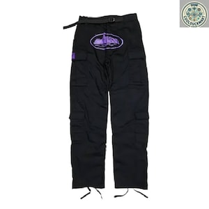 May include: Black cargo pants with multiple pockets and a black belt. The pants feature a purple oval design with a landscape graphic on the front. The pants have drawstrings at the ankles and a small purple square patch.