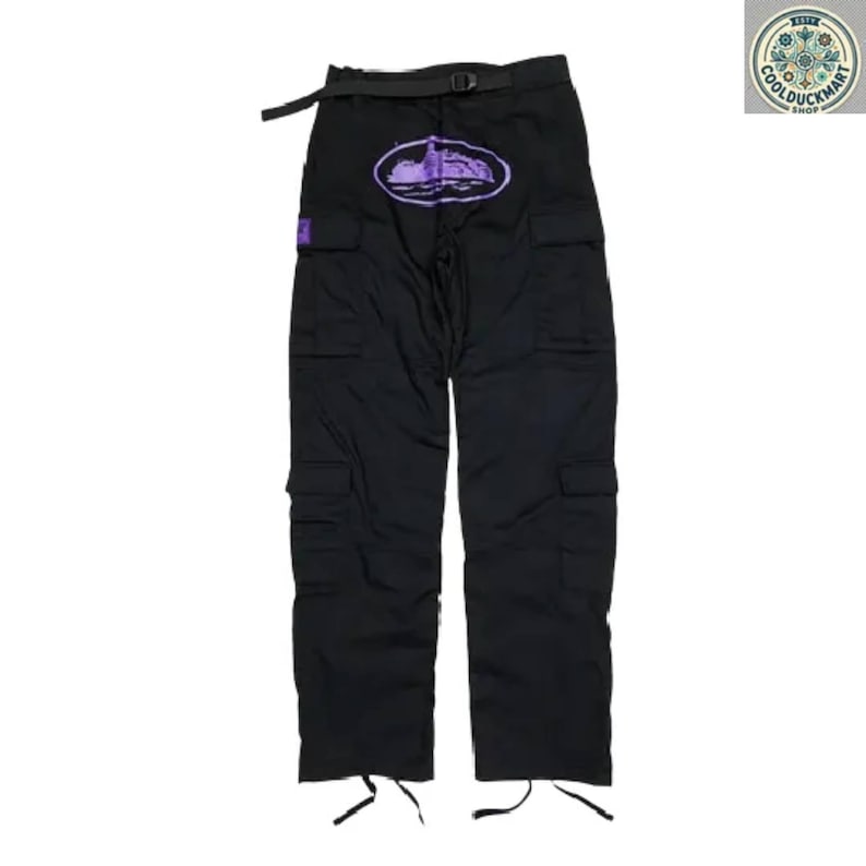 May include: Black cargo pants with multiple pockets and a black belt. The pants feature a purple oval design with a landscape graphic on the front. The pants have drawstrings at the ankles and a small purple square patch.