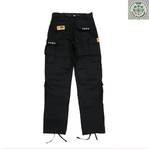 May include: Black cargo pants with multiple pockets and star details. The pants have a straight leg design and drawstrings at the ankles. Small yellow patches are visible on the pants.