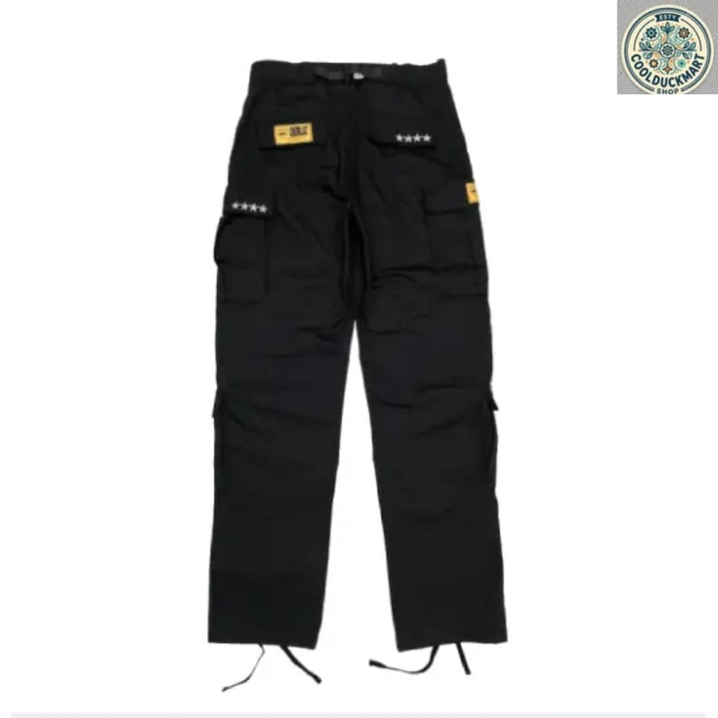 May include: Black cargo pants with multiple pockets and star details. The pants have a straight leg design and drawstrings at the ankles. Small yellow patches are visible on the pants.