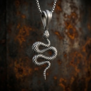 Peut inclure: Un pendentif en métal argenté en forme de serpent enroulé avec des textures d'écailles détaillées, suspendu à une chaîne carrée assortie. Le serpent est représenté dans une position verticale sinueuse avec une bélière lisse et effilée.