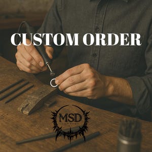 May include: A person in a dark grey shirt uses a rotary tool to polish a small silver ring on a wooden workbench. The text CUSTOM ORDER is displayed in white letters, and a black circular logo with the letters MSD is visible on the table.