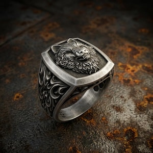 May include: A silver ring featuring a detailed relief of a snarling wolf head on the face. The band is crafted with intricate, swirling scrollwork patterns along the sides. The metal has a brushed, oxidized finish, and the number 925 is stamped.