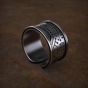 May include: A wide, open-ended silver ring featuring a dark, recessed circuit board pattern etched onto the outer surface. The interior of the band is smooth and clearly stamped with the hallmark 925, indicating sterling silver composition.