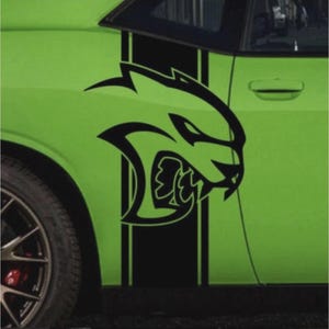 May include: A lime green car door featuring a black racing stripe and a black graphic of a snarling cat. The car has a black wheel with a red brake caliper.