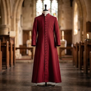 May include: A floor-length, deep red cassock featuring a high mandarin collar and a full-length front placket secured with a vertical row of matching fabric-covered buttons. The garment has long, straight sleeves and a structured, tailored fit.