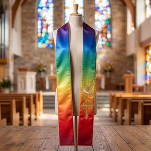 Op de afbeelding: Een liturgische stola met een levendig regenboogverloop van rood naar violet. De stof heeft een gladde, satijnachtige afwerking met een goudkleurige rand. Een geborduurde witte duif en een goudkleurig kruis bevinden zich op het linkerpaneel.