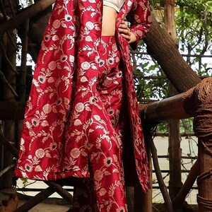 May include: A deep red long-sleeved jacket and matching trousers set featuring a repeating white floral pattern. The jacket has a notched collar and an open front, worn over a plain cream-coloured crop top. The fabric has a subtle sheen.