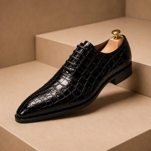 Può includere: Una scarpa oxford nera con un motivo testurizzato in pelle di coccodrillo lucida. La scarpa presenta una punta affusolata, lacci neri e un tacco basso. Un tendiscarpe in legno di colore chiaro è inserito per mantenerne la forma.