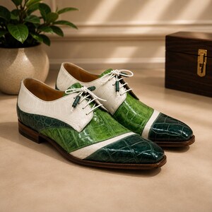 May include: A pair of lace-up oxford shoes featuring a two-tone design with white and green crocodile-embossed leather panels. The shoes have a pointed toe, a low wooden heel, and white laces with small green cylindrical aglets at the ends.