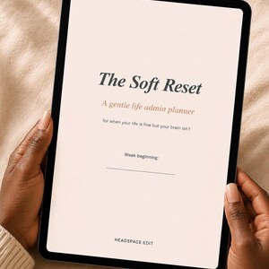 Puede incluir: Una tableta negra que muestra el texto "The Soft Reset" y "A gentle life admin planner". La tableta está sostenida por manos con uñas cuidadas. También se ve el texto "for when your life is fine but your brain isn't".
