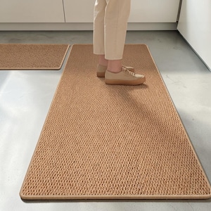 Op de afbeelding: Een rechthoekige, beige keukenloper met een getextureerd, geweven oppervlak en afgewerkte randen. Het kleed heeft een consistente, dichte luspoolconstructie in een neutrale aardetint, wat zorgt voor een vlak en uniform uiterlijk over de mat.