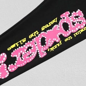 May include: Black fabric with the pink word "REBELS" in a bubble font, dotted with white circles. The phrases "never did the punk" and "heres the alive" are in yellow.