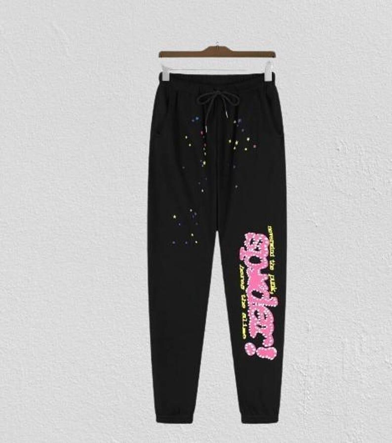 May include: Black sweatpants with a drawstring waist and pockets. The pants feature colorful splatter details and the text "powder!" in pink and yellow, with additional text in a script font.