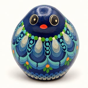 Könnte beinhalten: Eine abgerundete, eiförmige Figur mit einer glänzenden dunkelblauen Grundfarbe. Sie hat große schwarze Augen mit weißen Glanzlichtern und einen kleinen orangefarbenen Schnabel. Die Oberfläche ist mit komplizierten Mustern aus hellblauen, grünen und weißen Tropfenformen, Kreisen und kleinen orangefarbenen Punkten verziert.