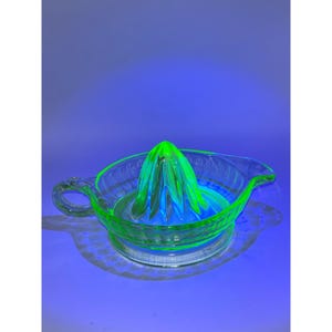 Peut inclure: Presse-agrumes vintage en verre transparent, d'une teinte vert vif sous une lumière bleue. Le presse-agrumes est doté d'un presse-agrumes rainuré et d'une poignée, conçu pour les agrumes. Le verre a une légère lueur.