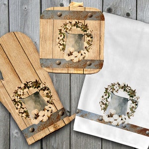 Könnte beinhalten: Set aus drei Küchentüchern mit rustikalem Bauernhaus-Design mit einem Kranz aus Baumwollknäueln und einem Metallkrug. Das Set beinhaltet einen Topflappen, ein Geschirrtuch und einen Topflappen.