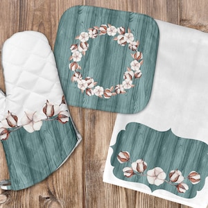 Puede incluir: Un juego de cocina con un guante de horno blanco, un salvamanteles cuadrado y un paño de cocina blanco. Cada artículo tiene un diseño de vetas de madera verde azulado con una rama de algodón y un patrón acolchado blanco. El salvamanteles tiene un diseño de corona de algodón.