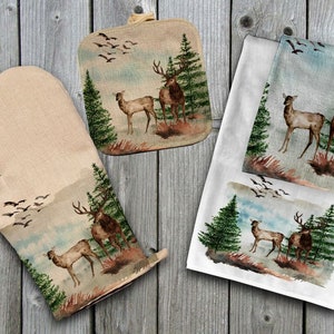 Puede incluir: Un juego de cocina con un diseño de acuarela de ciervos en una escena de bosque. El juego incluye un guante de horno beige, un salvamanteles cuadrado y un paño de cocina blanco. La obra de arte representa ciervos, árboles de hoja perenne y pájaros volando.