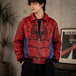 May include: Red and blue leather jacket with a Spider-Man web design. The jacket features a black spider emblem on the chest and a zipper closure. The jacket has a black collar and cuffs.