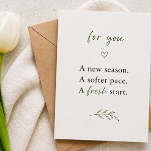 Può includere: Un biglietto di auguri bianco con le parole "for you" e il messaggio "A new season. A softer pace. A fresh start." è posto su una busta beige e un panno bianco. A sinistra c'è un tulipano bianco con foglie verdi.