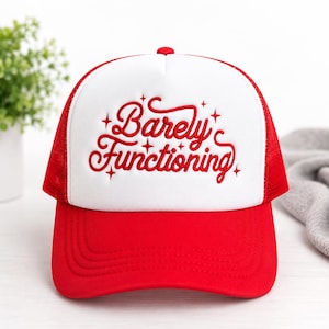May include: A red and white trucker hat featuring a white foam front panel with the red embroidered text Barely Functioning surrounded by small star accents. The hat has a red brim and red mesh side and back panels with a button on top.