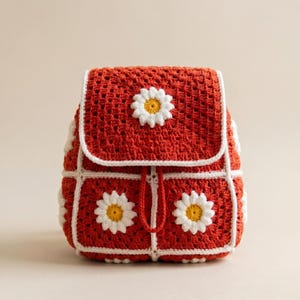 Può includere: Uno zaino rosso all'uncinetto fatto a mano con bordi bianchi e decorazioni a margherita. La borsa ha una chiusura con patta e un cordoncino, con tre applicazioni di margherite sul davanti. Le cuciture all'uncinetto sono visibili.