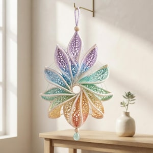 May include: A hanging wall decoration featuring a circular, multi-petaled flower shape made of crocheted yarn in a gradient of pastel colors including purple, blue, green, yellow, and orange. It includes a wooden bead and a hanging loop.