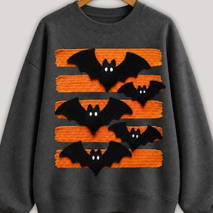 Halloween bat design in PNG format with black bats and orange patterned lines displayed on comfy t-shirt samples in charcoal, brown, olive green, rusty orange and cream for sublimation printing for the horror season and DTF t-shirts.