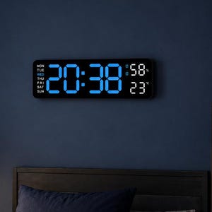 Op de afbeelding: Een rechthoekige digitale wandklok met een zwarte rand en een helderblauw led-display dat de tijd 20:38, de dagen van de week, een luchtvochtigheid van 58% en een temperatuur van 23 graden Celsius weergeeft op een donkerblauwe muur.