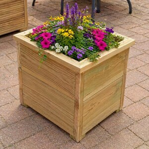 May include: A square wooden planter filled with vibrant flowers. The flowers are a mix of pink, purple, yellow, and white. The planter is made of light-coloured wood and sits on a brick patio.