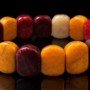 Può includere: Un braccialetto elastico composto da perline lisce, rettangolari e dai bordi arrotondati in colori alternati rosso intenso, giallo dorato e bianco crema. Le perline sono disposte in un motivo ripetitivo che forma una fascia circolare.