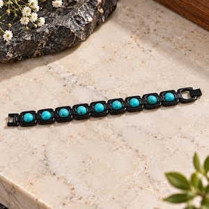 Könnte beinhalten: Ein Armband mit einer Reihe von quadratischen Gliedern aus schwarzem Metall, die jeweils eine runde, leuchtend türkisfarbene Perle enthalten. Die Glieder sind linear miteinander verbunden und bilden einen Kontrast zwischen dem dunklen Metall und den blauen Steinen.