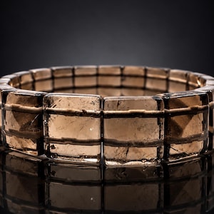 May include: A stretch bracelet composed of rectangular, translucent brown smoky quartz beads. Each bead features a horizontal etched line across the center, creating a uniform, linked appearance with a polished, reflective surface finish.
