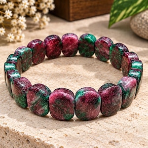 Pode incluir: Uma pulseira elástica composta por contas polidas de formato retangular com um padrão marmorizado em tons de magenta profundo, vermelho escuro e verde floresta. As contas estão dispostas num círculo contínuo, exibindo variações naturais.