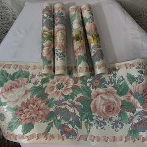 May include: Floral wallpaper border and rolls. The wallpaper border features a repeating pattern of large pink and blue flowers with green leaves on a cream background. Four rolls of matching wallpaper are also present.