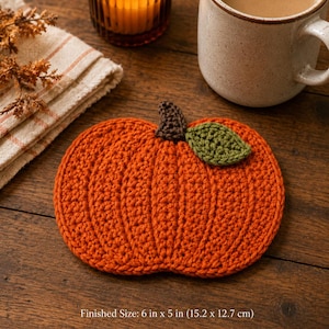 May include: A pumpkin-shaped crochet coaster in bright orange yarn with a dark brown stem and a single green leaf. The coaster measures 6 inches by 5 inches. The design features vertical ribbed stitching to mimic the texture of a pumpkin.