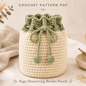 Puede incluir: Un bolso tipo saco con cordón de ganchillo que presenta una base de color crema y una sección superior de color verde salvia. El bolso incluye un cordón verde salvia con dos pequeños pompones esféricos en los extremos. El texto dice Crochet Pattern PDF y Sage Drawstring Bucket Pouch.