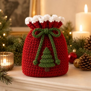 Könnte beinhalten: Ein roter Häkelbeutel mit Kordelzug, einem weißen, gewellten oberen Rand und einer grünen, gehäkelten Weihnachtsbaum-Applikation auf der Vorderseite. Der Beutel wird mit einer grünen Häkelkordel zu einer Schleife mit Knoten an den Enden verschlossen.