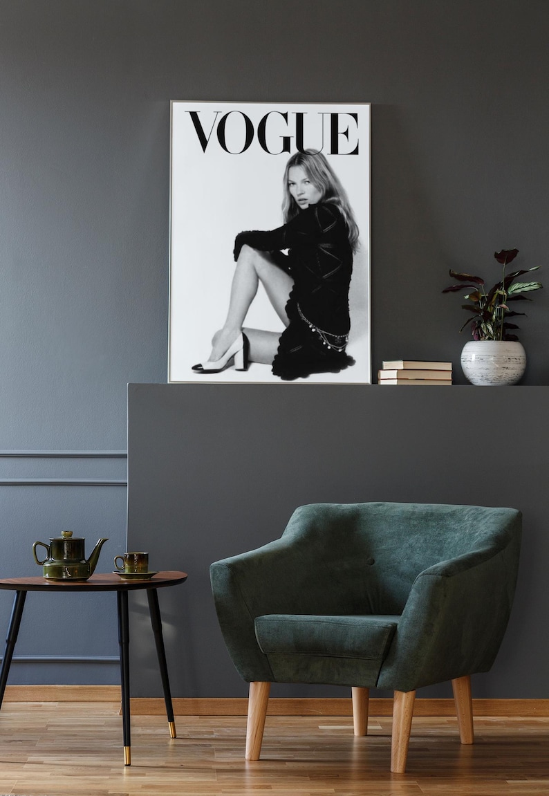 Puede incluir: Portada de la revista Vogue en blanco y negro con una modelo sentada con un vestido negro y tacones. La revista se muestra en una pared gris sobre un sill&oacute;n verde oscuro y una peque&ntilde;a mesa con una tetera y una taza.